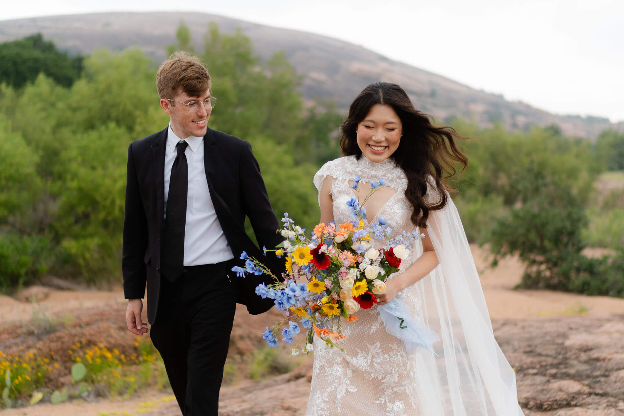 Bride and groom holding hands with Enchanted Rock granite dome in the background