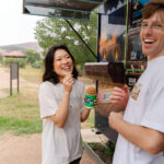 Couple sharing snow cones together after hiking together on Enchanted Rock summit trail during elopement day