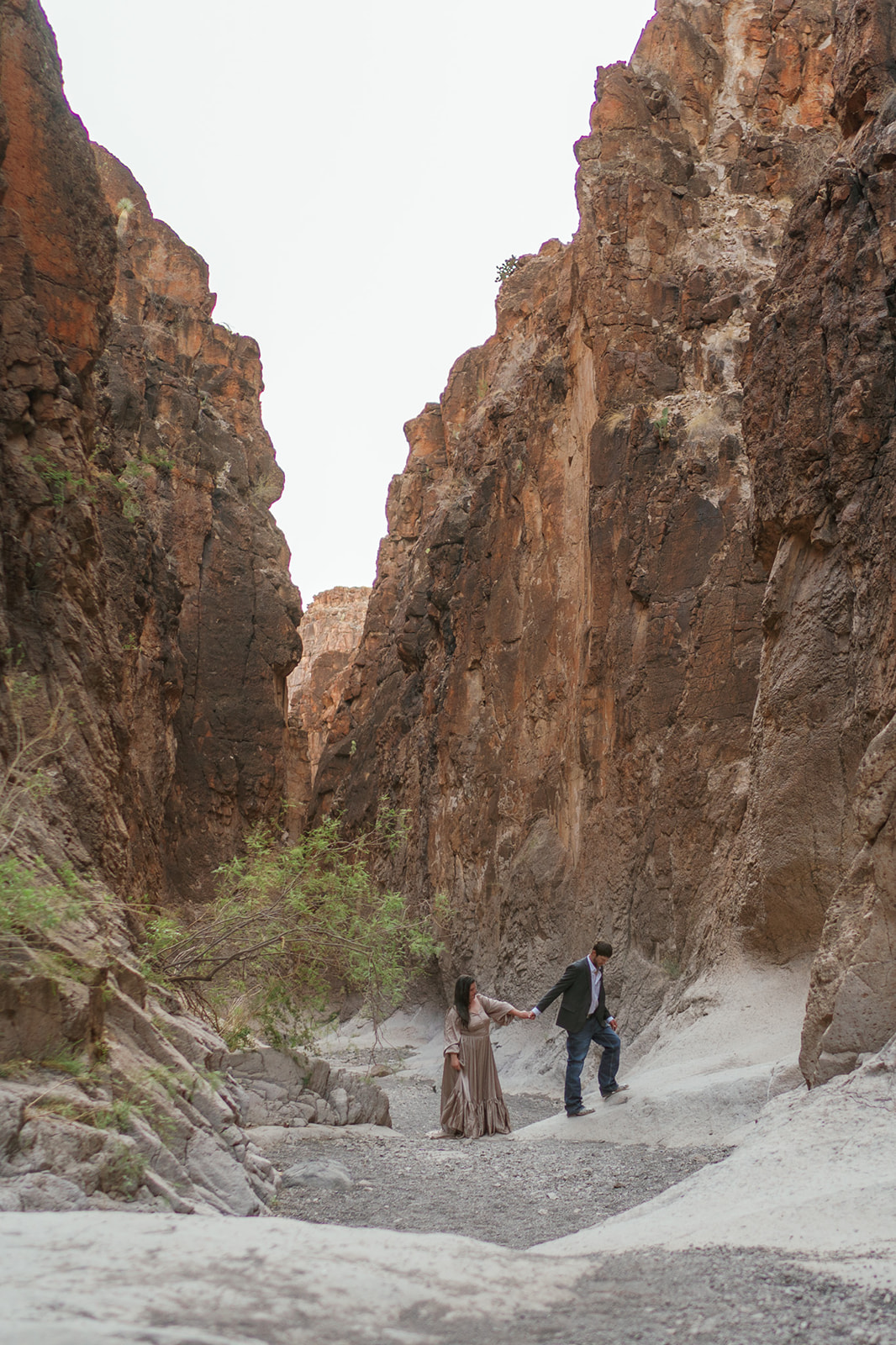 A groom leads his bride in a brown dress through a canyon by the hand during their Utah Elopement