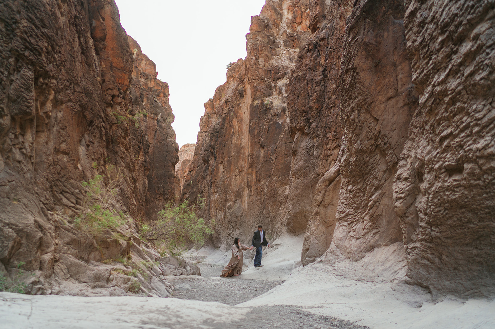 Newlyweds walk through a sandy canyon with steep wall hand in hand during their Utah Elopement