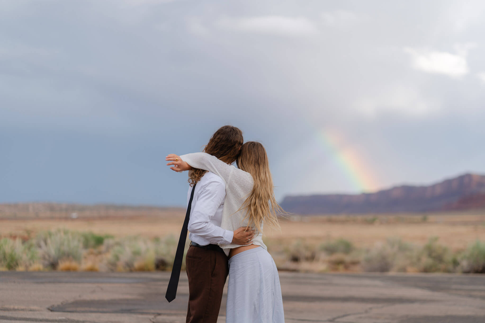 Couple dancing and embracing with a vibrant rainbow in the background at Moab desert