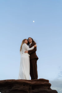 Couple embraces on rock formation at dead horse point wedding with the moon shining overhead