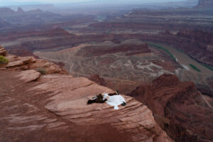 Couple laying together on the edge of Dead Horse Point overlook, surrounded by red rock canyons at sunset