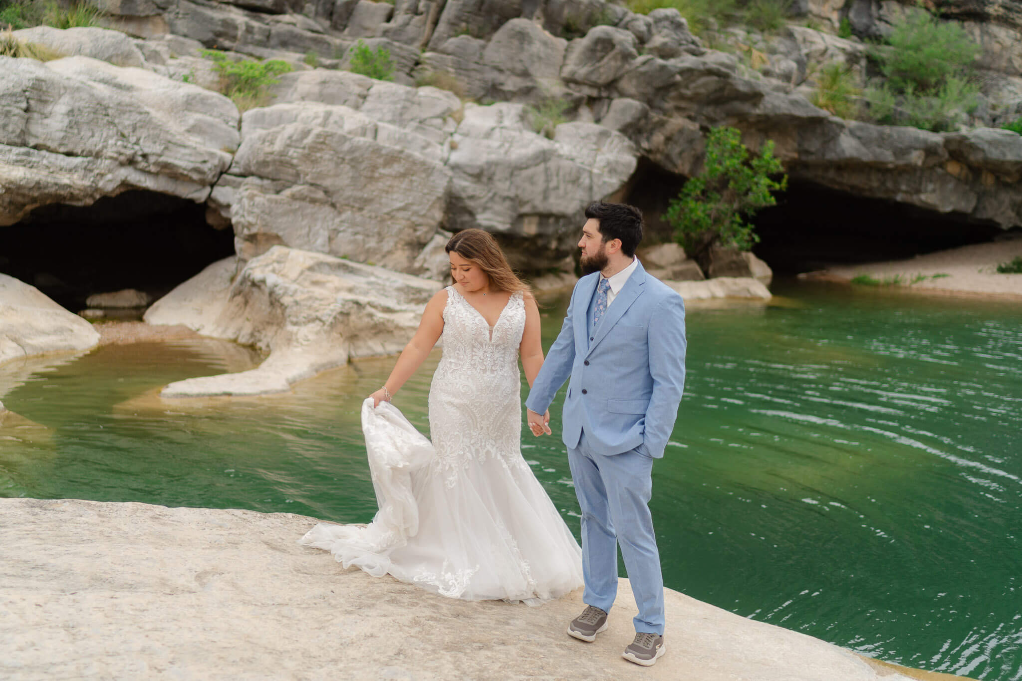 Bride and groom showing off their elopement outfits by a bright turquoise body of water