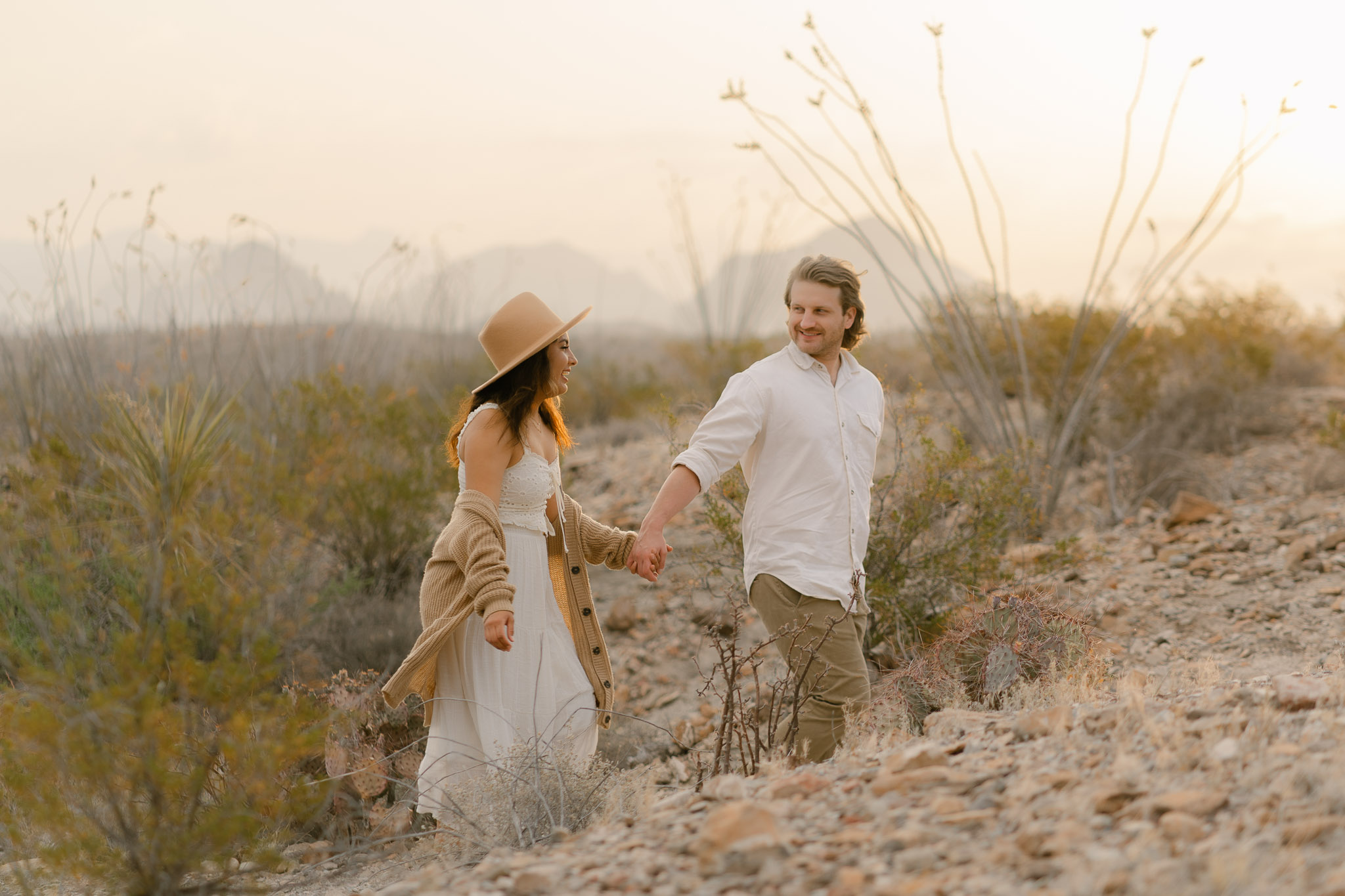 couple holding hands and walking through a desert landscape at sunrise