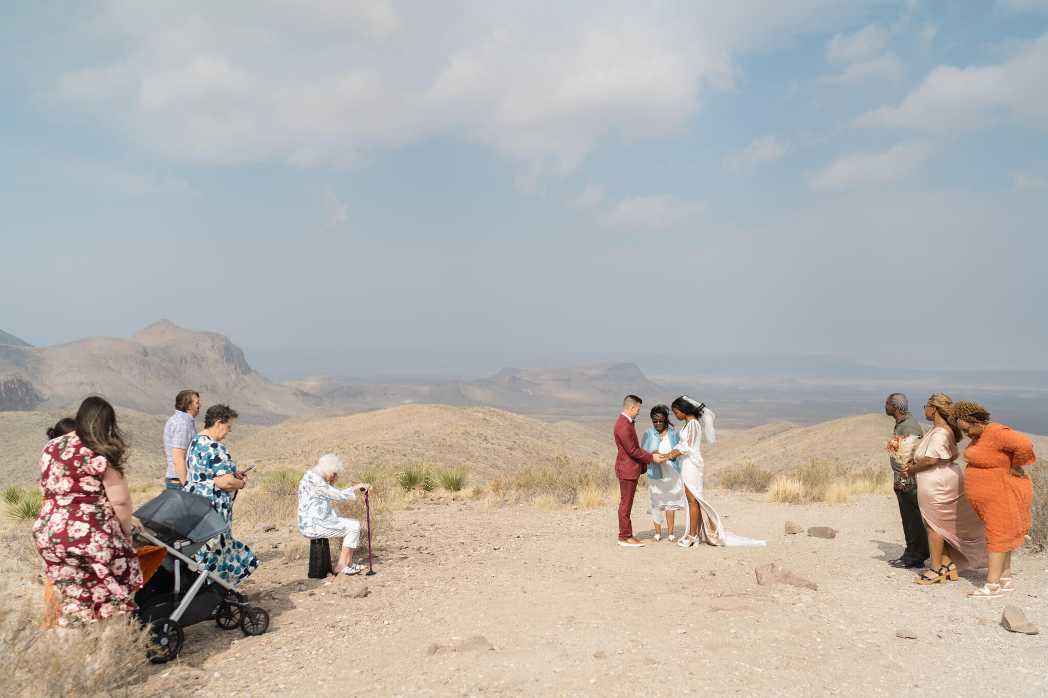 Couple standing on a viewpoint as their family watches their elopement ceremony