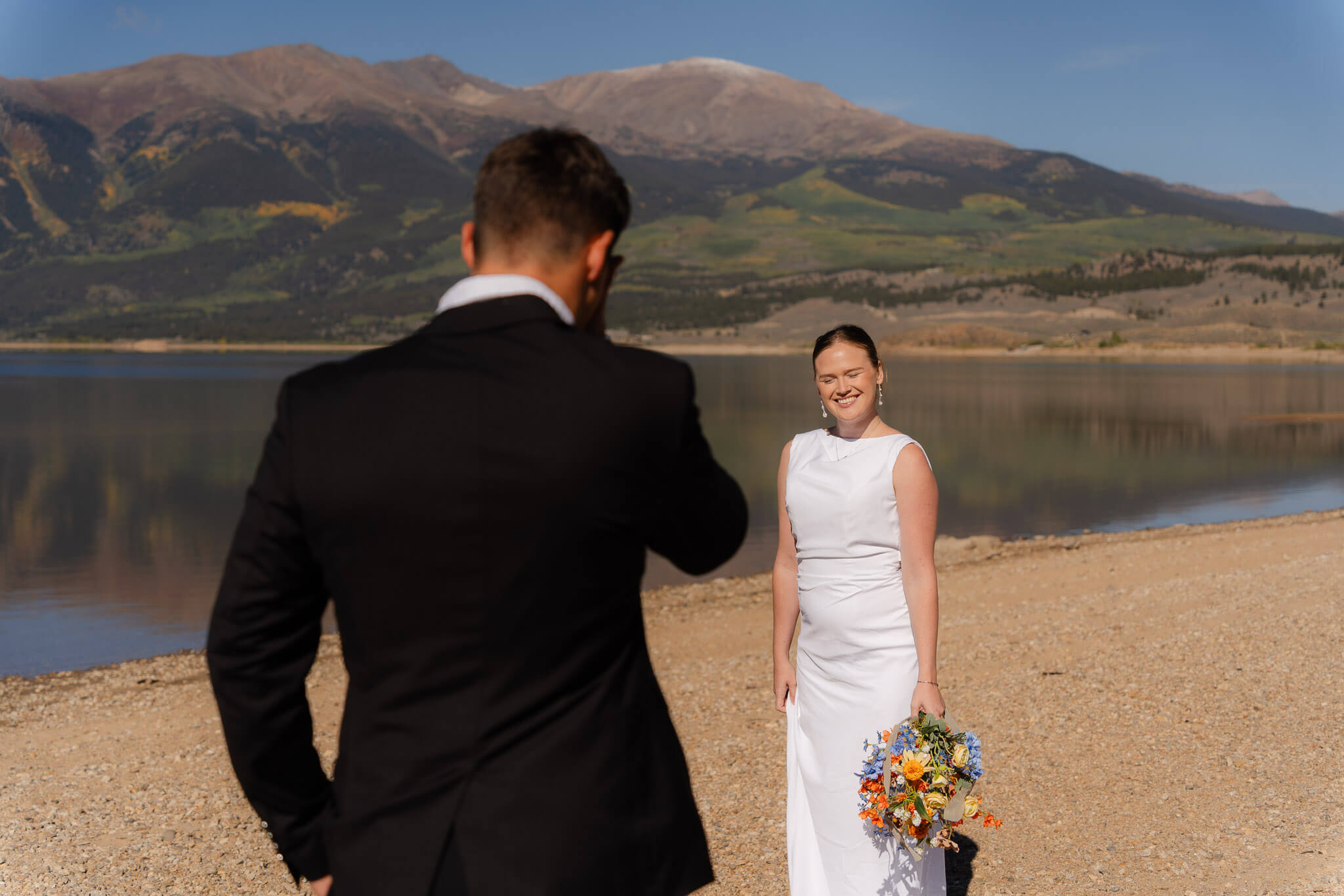 bride smiling at her groom next to a Colorado lake in the mountains