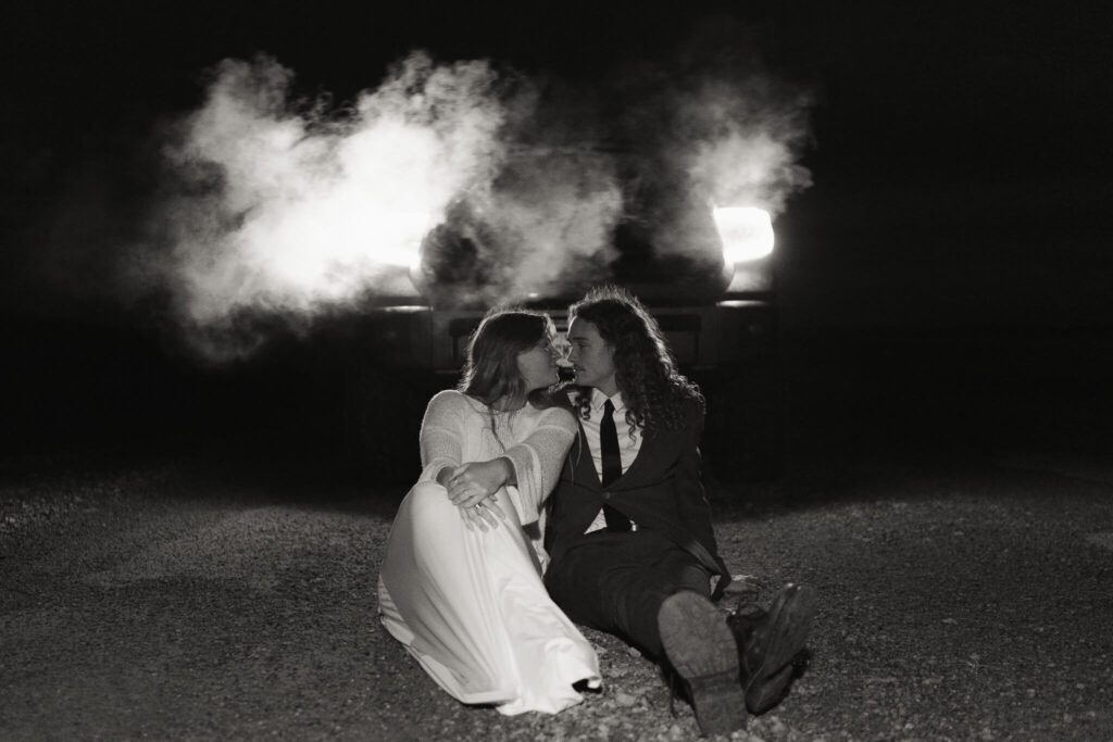 couple sitting in front of the headlights at the end of their elopement day
