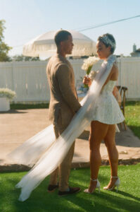 Documentary portrait of a bride in a structured sparkly mini dress and her partner at a lush green wedding, blending candid moments with green wedding inspiration.