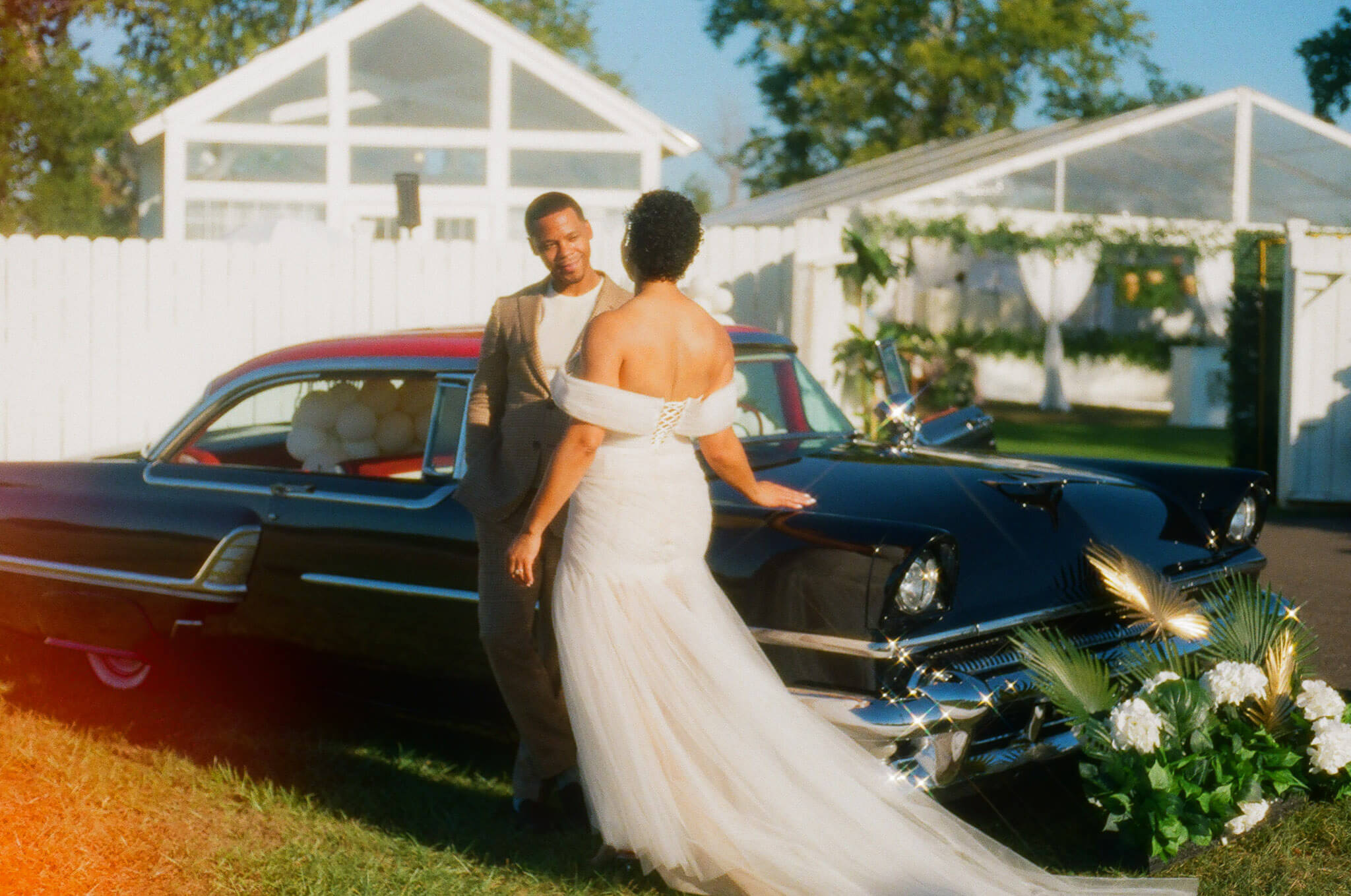 Documentary portrait of a bride and her partner in front of a vintage car at a lush green wedding, blending candid moments with green wedding inspiration.
